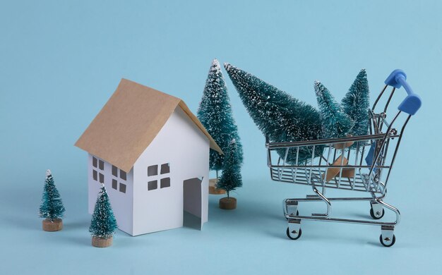 Modelo de casa y carro de la compra del árbol de Navidad sobre un fondo azul.