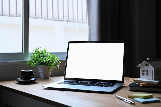 Modelo de casa de computadora portátil y taza de café en mesa de madera Hipoteca y concepto de inversión inmobiliaria