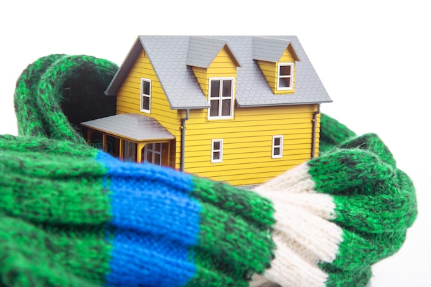El modelo de la casa está aislado con una bufanda de punto sobre un fondo blanco el concepto de mantener el calor y la comodidad en el interior de la casa con protección contra el frío