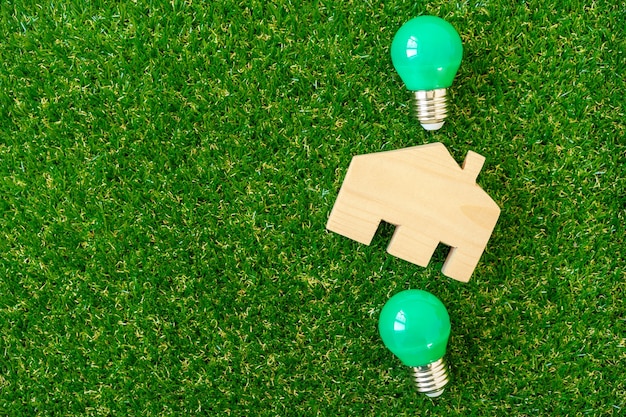 Foto modelo de casa de madera y bombilla sobre fondo verde