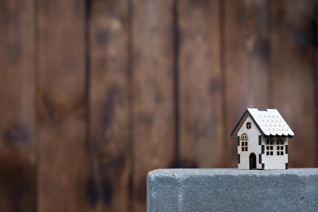 Modelo de una casa de madera con espacio de copia a la izquierda sobre el fondo de una pared de madera La casa se alza sobre una losa de hormigón el concepto de construir o comprar una casa