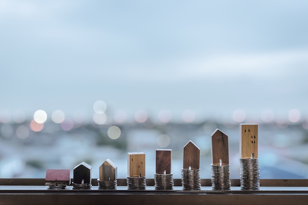 Foto modelo de casa de madera y fila de monedas en mesa de madera con fondo azul claro, real esta