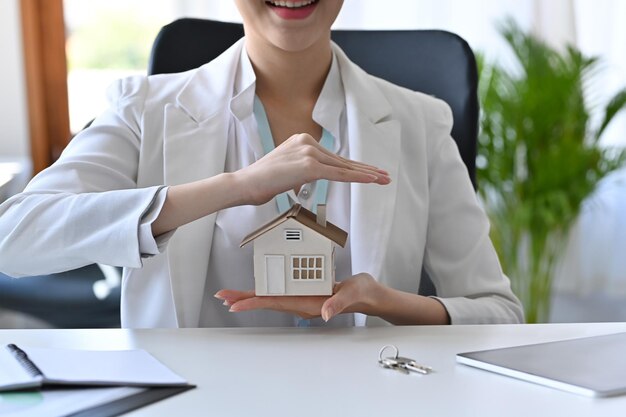 Modelo de casa de protección de mano de mujer joven de tiro recortado. Concepto inmobiliario de seguro o préstamo.