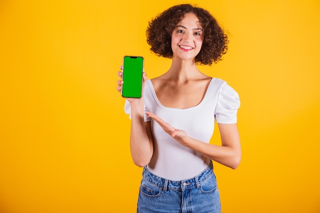 Modelo caucasiano vestindo uma camisa branca e calças de ganga azuis segurando um telefone celular com uma tela verde