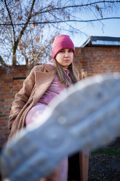 Modelo de chica elegante con un abrigo marrón, traje rosa y botas grises en las ruinas de la ciudad. Las tendencias de la moda moderna. Imagen de moda