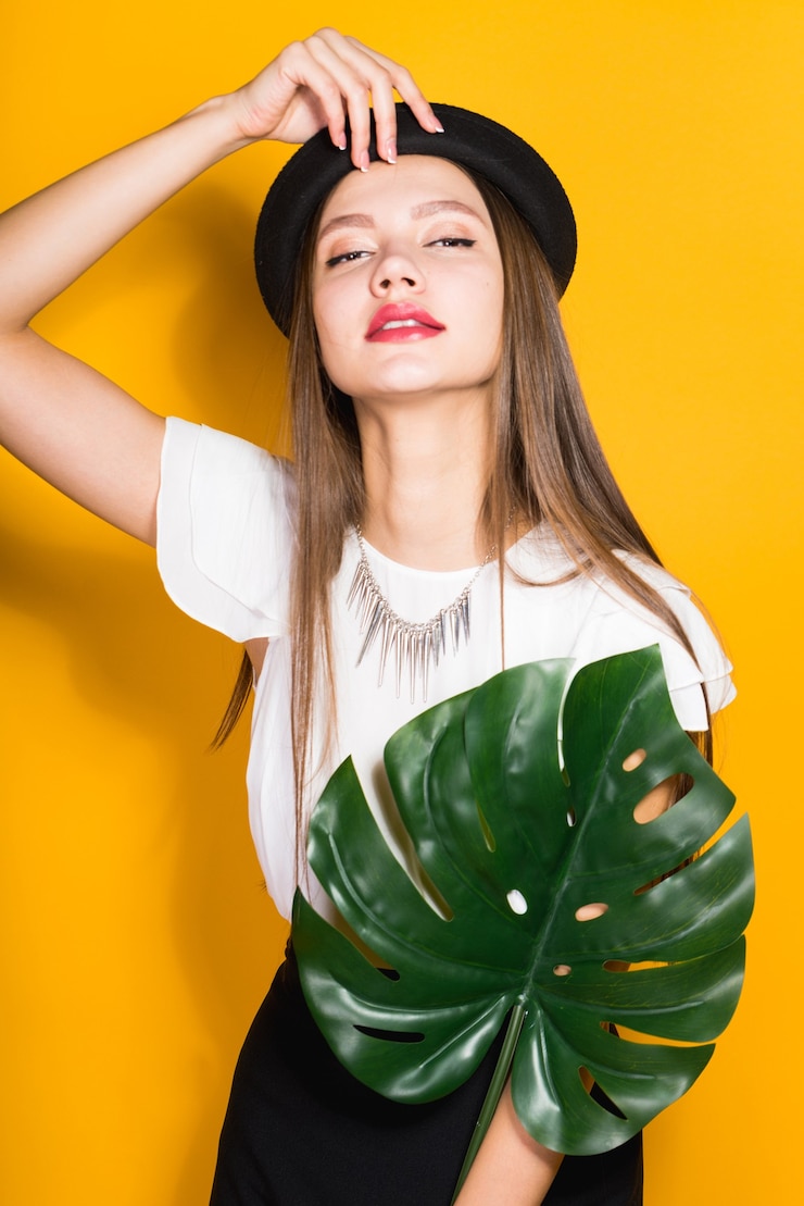 Foto modelo de chica con estilo seguro en un sombrero negro de moda tiene una hoja verde, plantea