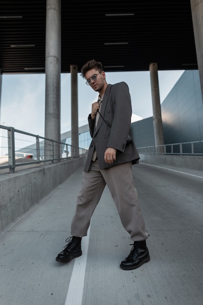 Modelo de chico elegante en un traje gris de moda con botas camina en la ciudad