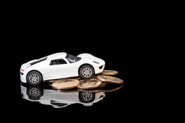 Modelo de coche blanco con un montón de monedas de oro sobre fondo reflectante negro