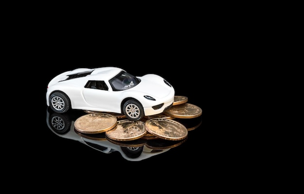 Modelo de coche blanco con un montón de monedas de oro sobre fondo reflectante negro