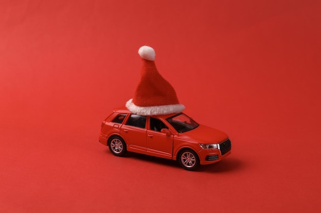 Modelo de coche de juguete con un sombrero de Papá Noel en un fondo rojo Concepto de Feliz Navidad