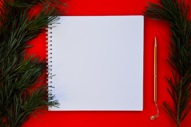 Modelo de Ano Novo e Natal Um caderno branco e uma caneta dourada repousam sobre um fundo vermelho