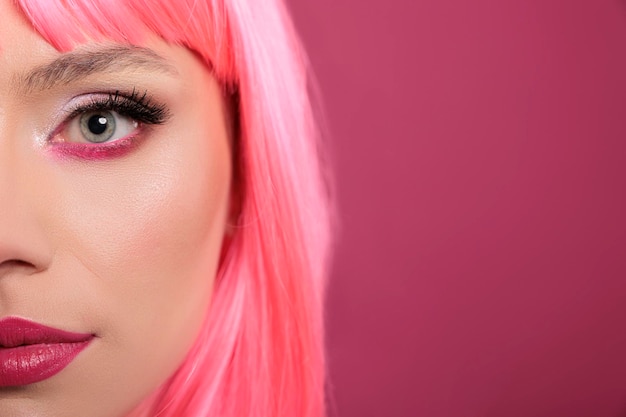 Modelo de beleza atraente mostrando metade do rosto na câmera no estúdio, com cabelo rosa e cosméticos de maquiagem. mulher bonita elegante se sentindo sensual e despreocupada, se divertindo sobre o fundo. fechar-se.