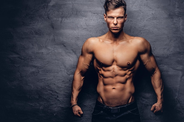 Modelo de belo jovem sem camisa com belo corpo musculoso posando em um estúdio. Isolado em um fundo escuro.