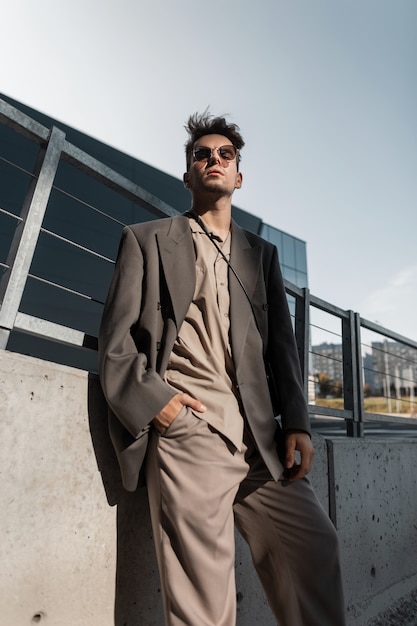 Modelo de cara elegante bonito empresário em moderno terno cinza com óculos de sol na cidade. Estilo urbano masculino