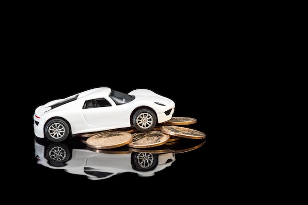 Modelo de carro branco com monte de moedas de ouro sobre fundo reflexivo preto