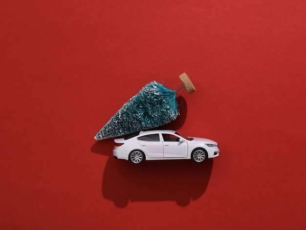 Foto modelo de carro de brinquedo com árvore de natal em fundo vermelho entrega de conceito de feliz natal