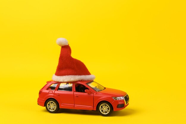 Foto modelo de carro de brinquedo com chapéu de papai noel em fundo amarelo feliz natal