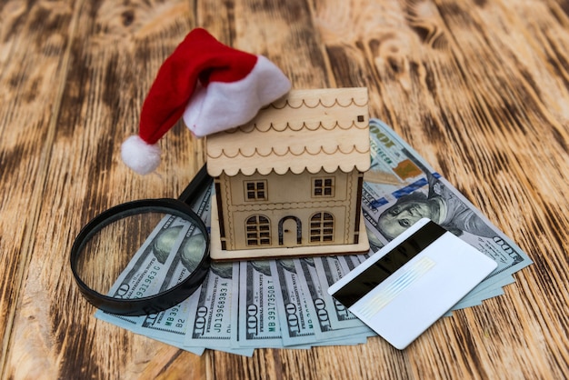 Modelo de casa de madeira com chapéu de papai noel e notas de dólar