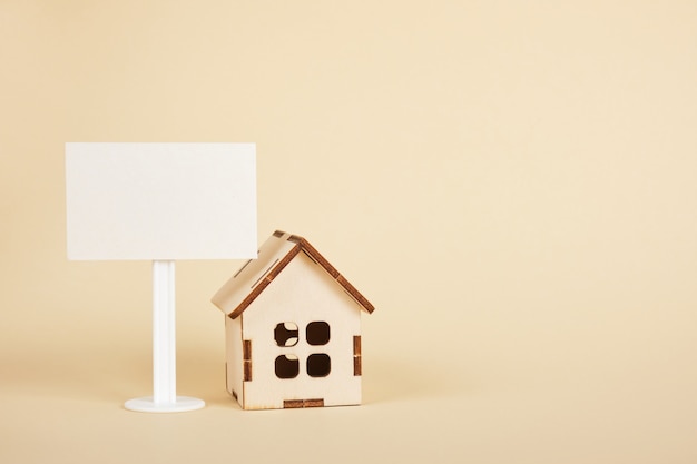 modelo de casa de madeira e placa branca em branco sobre fundo bege cópia espaço conceito imobiliário
