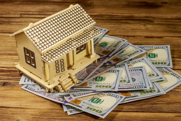 Modelo de casa e notas de cem dólares americanos em fundo de madeira Conceito imobiliário de hipoteca de hipoteca de casa de investimento imobiliário