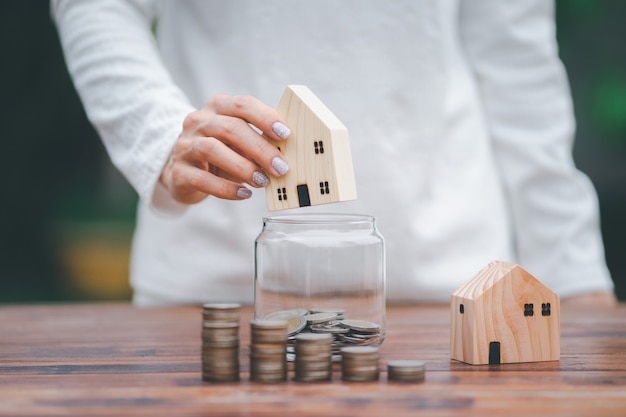 Foto modelo de casa em mãos com a colocação de moedas na etapa de crescimento crescente do frasco, economizando dinheiro, pilha de dinheiro em primeiro plano