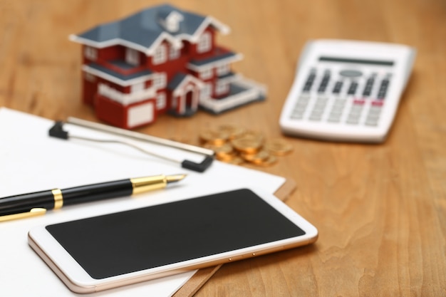 Foto modelo de casa, smartphone, calculadora e moedas de ouro na mesa de madeira