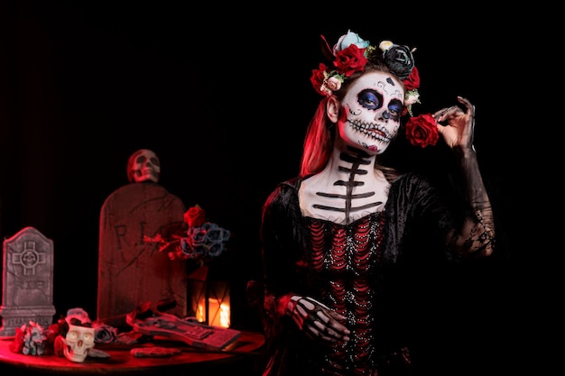 Modelo de deusa assustadora com maquiagem festival usando coroa de flores e traje tradicional glamour dios de los muertos. Segurando rosa e posando na celebração da cultura do feriado mexicano.