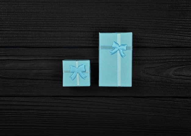 Modelo de dia dos namorados de duas pequenas caixas de presente azuis fechadas com laços de fita sobre o fundo da mesa de madeira preta, close-up plano, vista superior elevada, diretamente acima