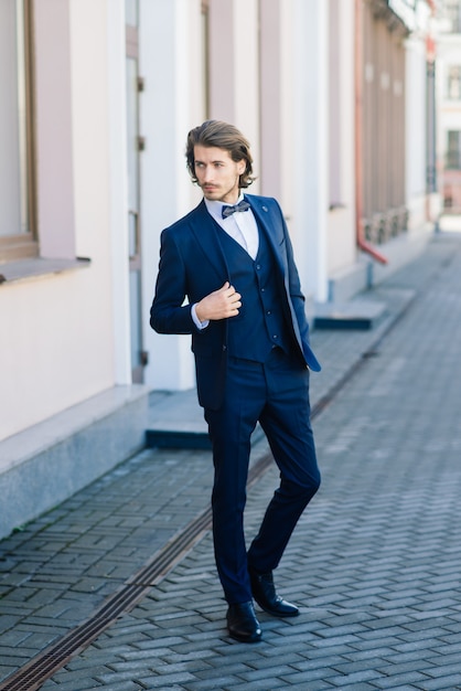 Modelo de empresário de moda bonito vestido com um terno elegante e posando na rua. Metrossexual