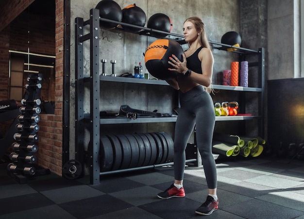 Modelo de fitness feminino jovem exercitando-se com medicine ball no ginásio. Mulher caucasiana, fazendo exercícios de crossfit.