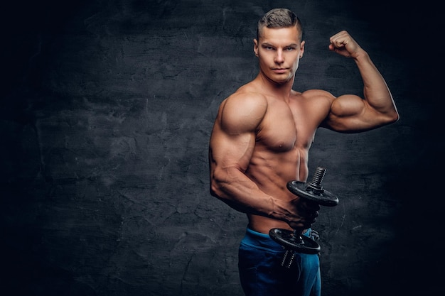 Modelo de fitness masculino jovem bronzeado abdominal sem camisa detém haltere em fundo cinza.