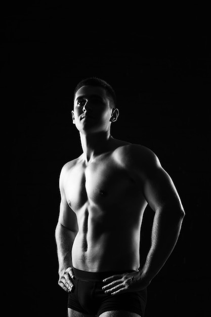 Modelo de fitness masculino mostrando músculos em estúdio com fundo preto