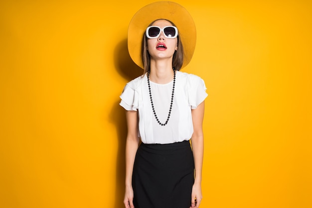 Modelo de garota jovem elegante confiante em óculos de sol e vestido grande posando em fundo amarelo