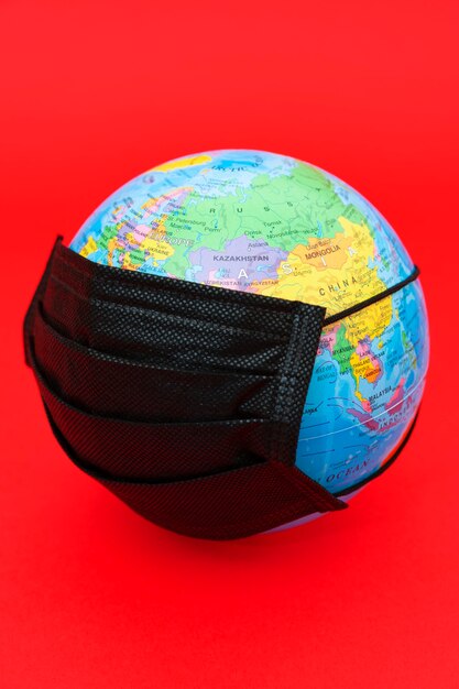 Modelo de globo terrestre com máscara cirúrgica preta isolada em fundo vermelho