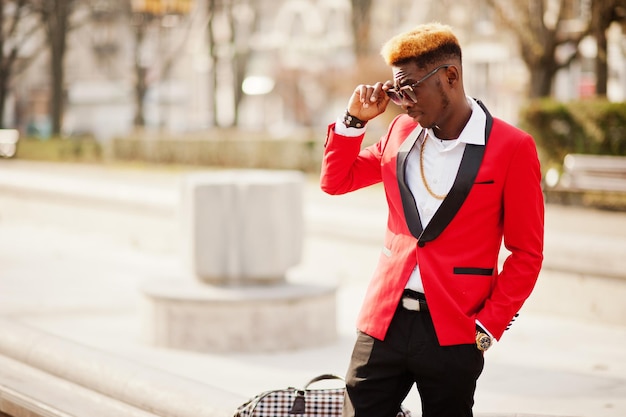 Modelo de homem afro-americano de moda em terno vermelho com cabelo de destaques e bolsa posada na rua