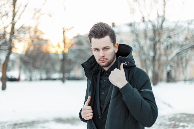 Modelo de jovem bonito com cabelo em uma jaqueta preta em um parque nevado