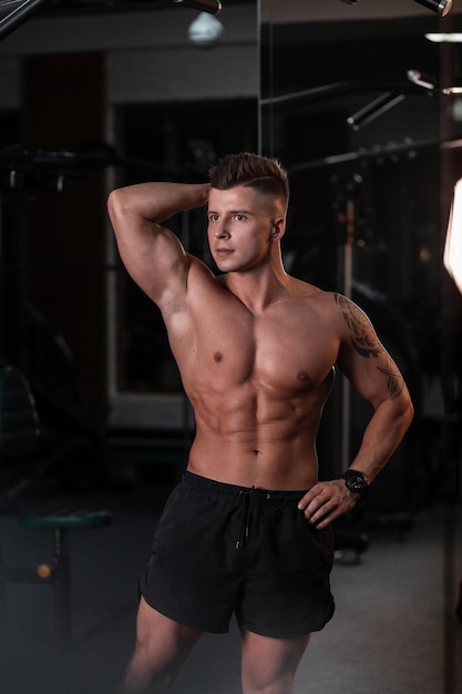 Modelo de jovem esportivo bonito com um torso nu muscular esbelto posa e treina no ginásio