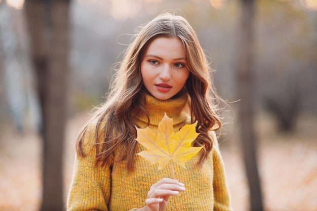 Modelo de jovem no parque de outono com folhas de bordo de folhagem amarela, moda da temporada de outono
