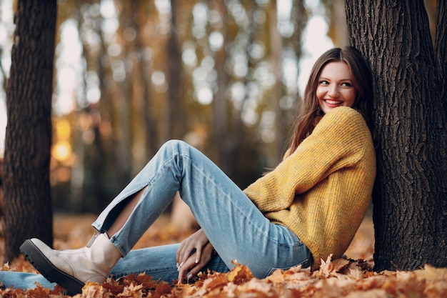 Modelo de jovem no parque de outono com folhas de bordo de folhagem amarela, moda da temporada de outono