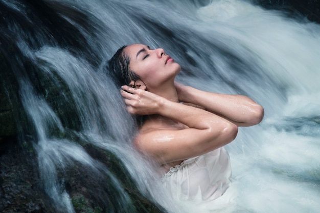 Foto modelo de linda mulher asiática posando sob a cachoeira usando swimwear branco
