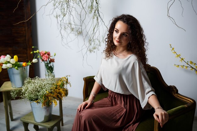 Modelo de menina bonita com cachos em um vestido posando em belos arranjos. O início da primavera com flores