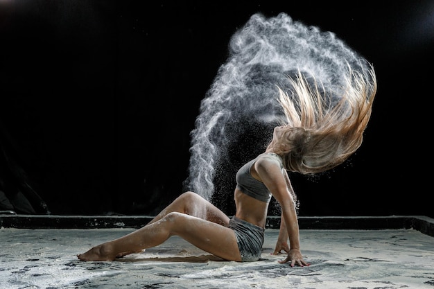 Modelo de menina bonita em um fundo preto joga farinha