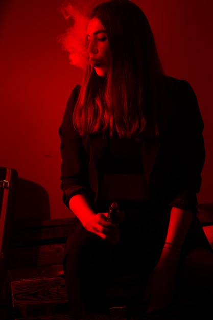 Foto modelo de menina fuma vape em luz vermelha.