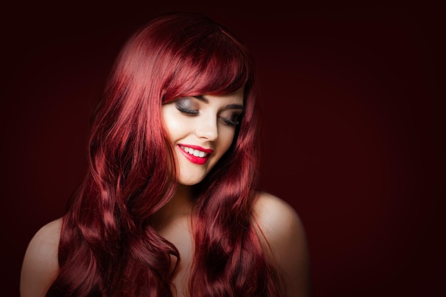 Modelo de moda de mulher ruiva sorridente em fundo vermelho escuro maquiagem penteado ondulado perfeito