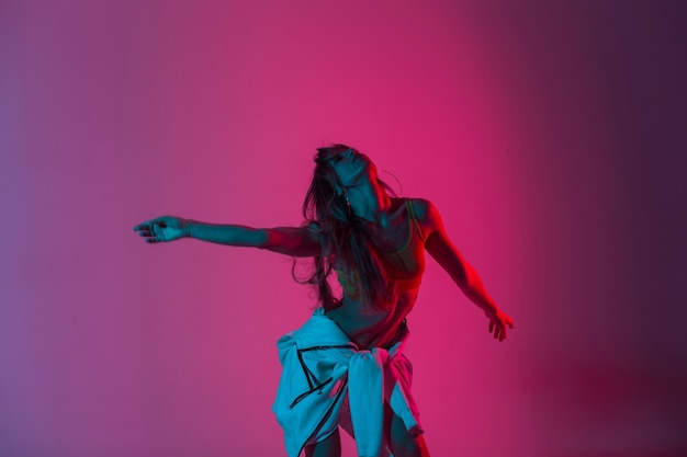 Modelo de moda jovem bonita moderna com roupas elegantes, posando em uma sala com glitter colorido. Bela dançarina de garota sexy relaxa e dançando dentro de casa um néon rosa brilhante no estilo discoteca.