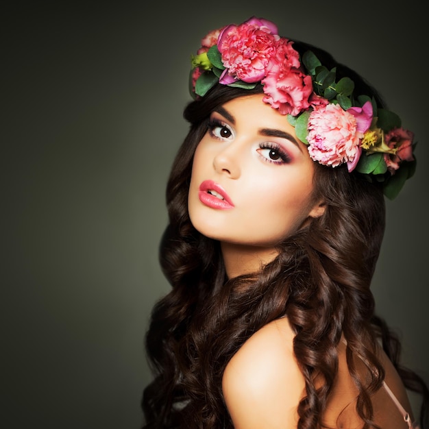 Modelo de moda mulher bonita com maquiagem e flores em plano de fundo à noite. Penteado cacheado perfeito, maquiagem e grinalda de flores