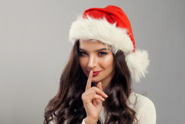 Modelo de mulher de Natal usando chapéu de Papai Noel vermelho segurando o dedo nos lábios