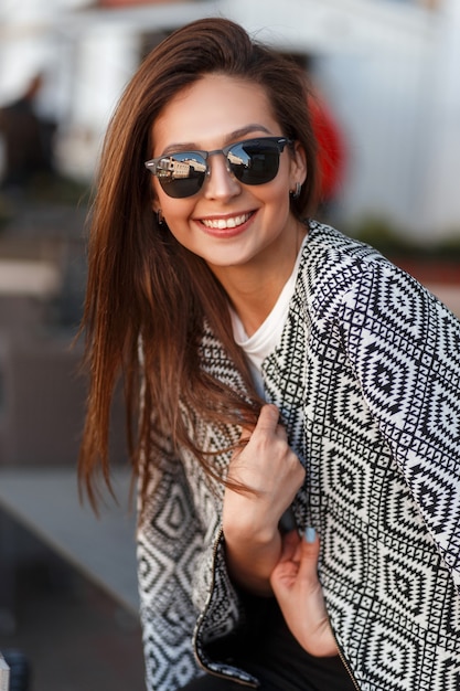 Modelo de mulher feliz com um sorriso e óculos de sol da moda em um café na cidade