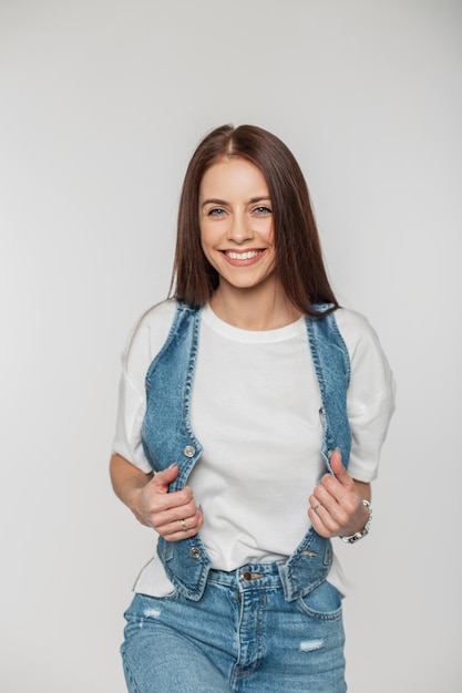 Modelo de mulher jovem e bonita feliz com um sorriso fofo em roupas jeans da moda em um retrato de fundo branco de uma menina sorridente