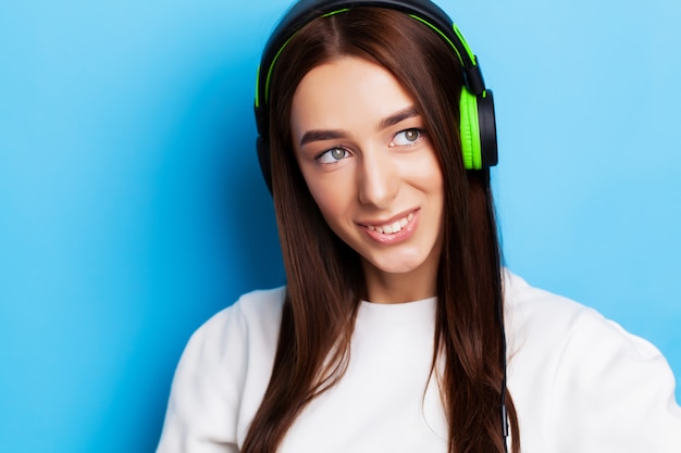 Modelo de mulher jovem e bonita ouve música em fones de ouvido em azul